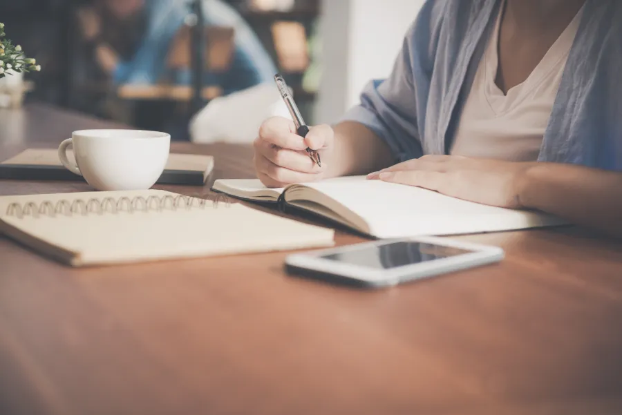 Woman writing on a notebook beside a laptop
